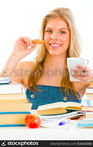 Smiling teen girl sitting at table with books and drinking tea with cookie&#xA;