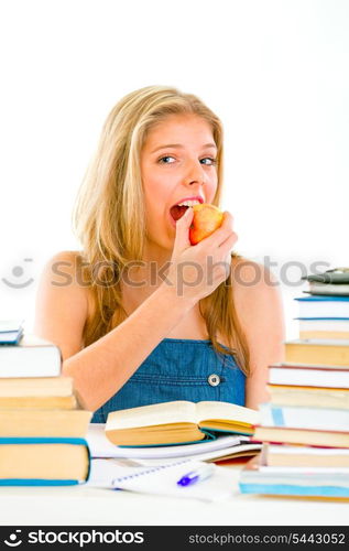 Smiling teen girl sitting at table with books and eating apple&#xA;