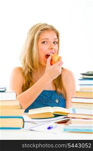 Smiling teen girl sitting at table with books and eating apple&#xA;
