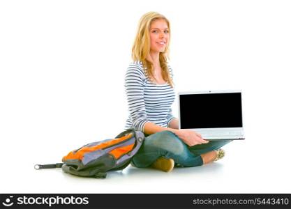 Smiling teen girl sitting on floor and showing laptops blank screen isolated on white &#xA;