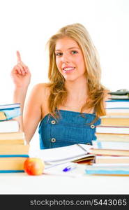 Smiling teen girl with rised finger sitting at table with books. Idea gesture &#xA;