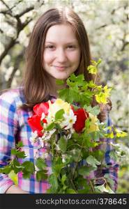 smiling teen girl with the bouquet of spring flowers at the blooming garden