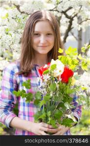 smiling teen girl with the bouquet of spring flowers at the blooming garden
