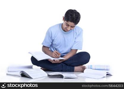 Smiling teenage boy sitting on floor cross-legged studying against white background
