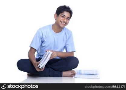 Smiling teenage boy sitting on floor with books against white background