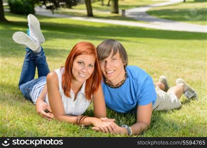Smiling teenage couple lying in sunny park enjoy first love