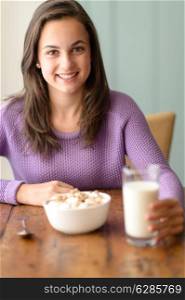Smiling teenage girl enjoy healthy cereal breakfast and glass of milk