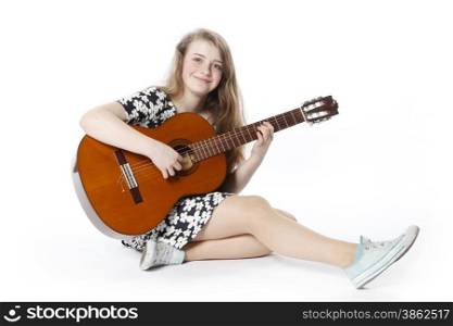 smiling teenage girl in dress plays the guitar in studio sitting on the floor