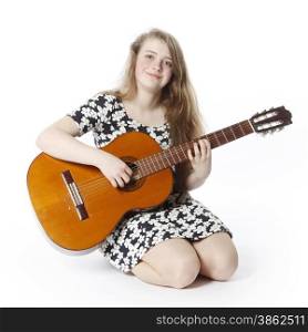 smiling teenage girl in dress plays the guitar in studio with white background sitting on the floor