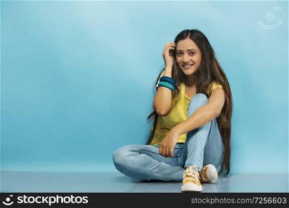 Smiling teenage girl in jeans and t-shirt sitting on the floor and posing for photograph