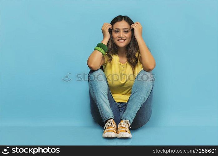 Smiling teenage girl in jeans and t-shirt sitting on the floor with her hands resting on her knees