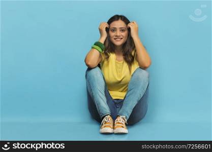 Smiling teenage girl in jeans and t-shirt sitting on the floor with her hands resting on her knees