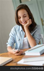 Smiling teenage girl looking at mobile phone studying at home