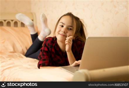 Smiling teenage girl lying on bed and using laptop