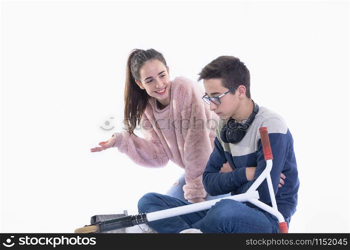 Smiling teenage girl on her knees tries to cheer up a boy sitting cross-legged with an angry expression on a light background. Friendship concept.. Smiling teenage girl tries to cheer up an angry boy