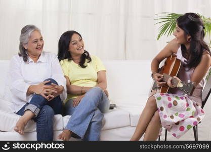 Smiling teenage girl playing guitar for her mother and grandmother