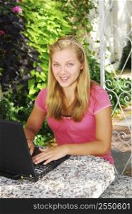 Smiling teenage girl typing on a portable computer outside