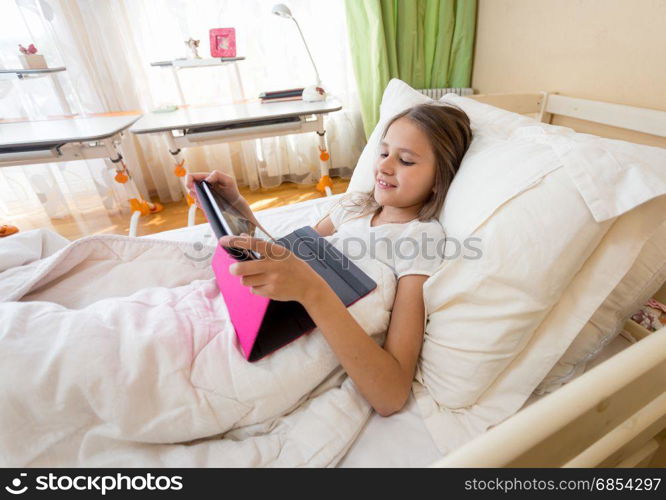 Smiling teenage girl using digital tablet at bed