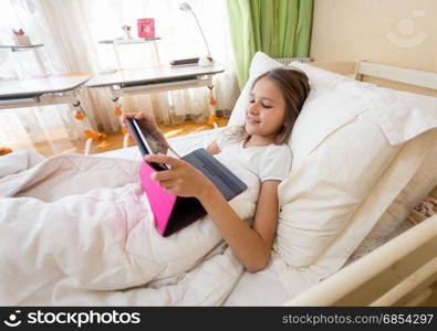 Smiling teenage girl using digital tablet at bed