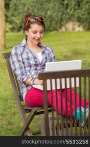 Smiling teenage girl using laptop sitting on chair at park