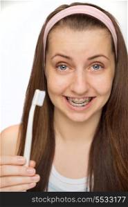 Smiling teenage girl wearing braces showing toothbrush on white background