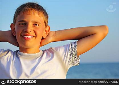 smiling teenager boy against sea, holding hands behind head