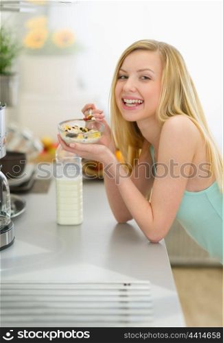 Smiling teenager girl eating breakfast in kitchen