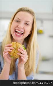 Smiling teenager girl eating sandwich in kitchen