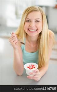 Smiling teenager girl eating yogurt in modern kitchen