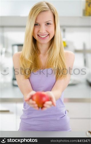 Smiling teenager girl giving apple in kitchen