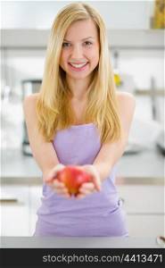 Smiling teenager girl giving apple in kitchen