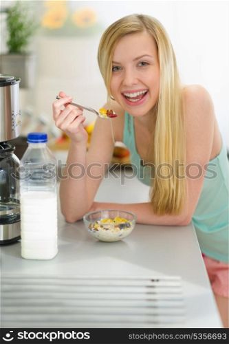 Smiling teenager girl having breakfast eating flakes with milk