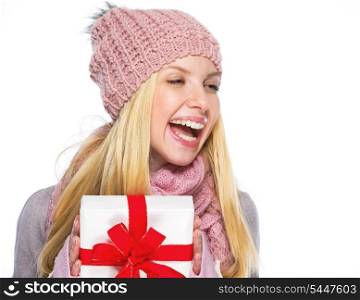 Smiling teenager girl in winter hat and scarf with presenting box looking on copy space