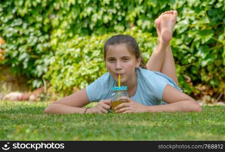 smiling teenager girl lying in the grass and drinking orange juice