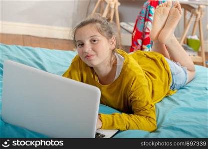 smiling teenager girl lying on the bed, using a laptop