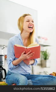 Smiling teenager girl reading book in kitchen