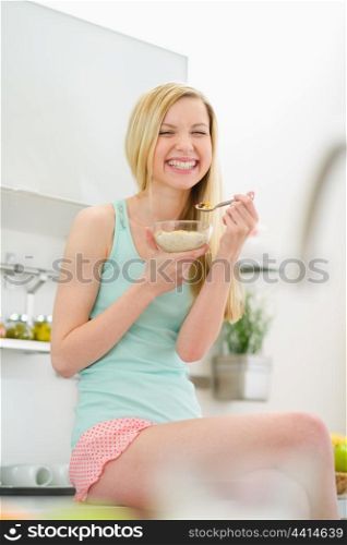 Smiling teenager girl sitting in kitchen and eating flakes with milk