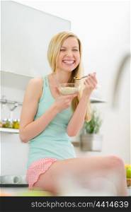 Smiling teenager girl sitting in kitchen and eating flakes with milk