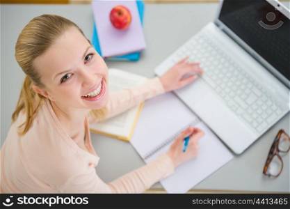 Smiling teenager girl studying in kitchen