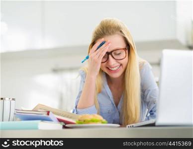 Smiling teenager girl studying in kitchen