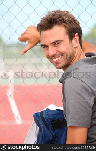 Smiling tennis player standing outside a hard court