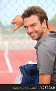 Smiling tennis player standing outside a hard court