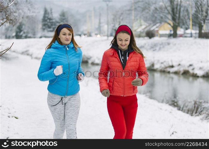 smiling two female friends jogging winter season