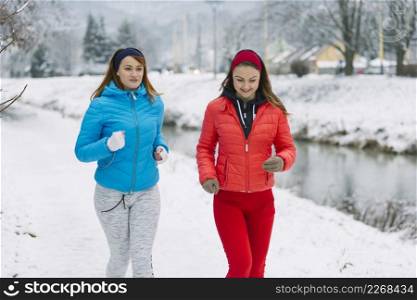 smiling two female friends jogging winter season