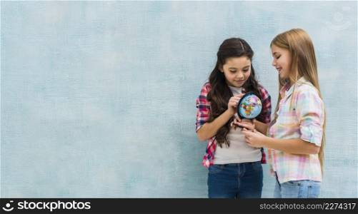 smiling two girls standing against blue wall looking small globe
