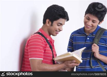 Smiling university students reading book against wall