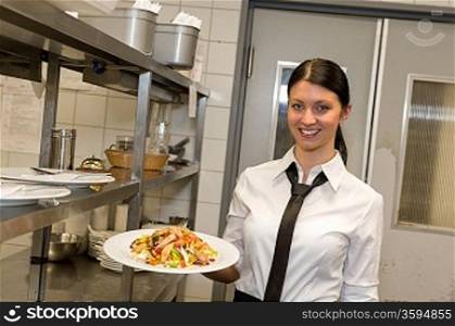Smiling waitress serving salad on plate in restaurant&acute;s kitchen