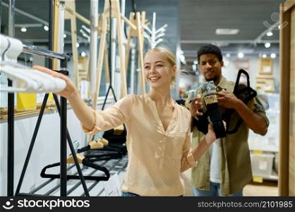 Smiling wife walking with clothes hanger pack. Interracial married couple buyer at furniture market. Interracial married couple buyer at furniture market