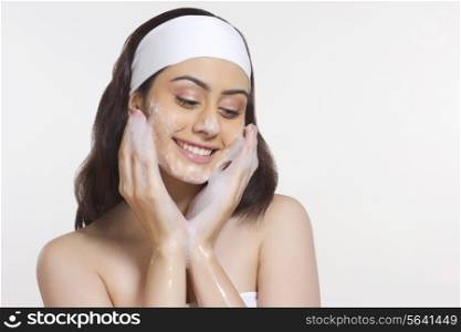 Smiling woman applying soap on face against white background
