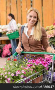 Smiling woman buying flowers in garden center pushing shopping cart